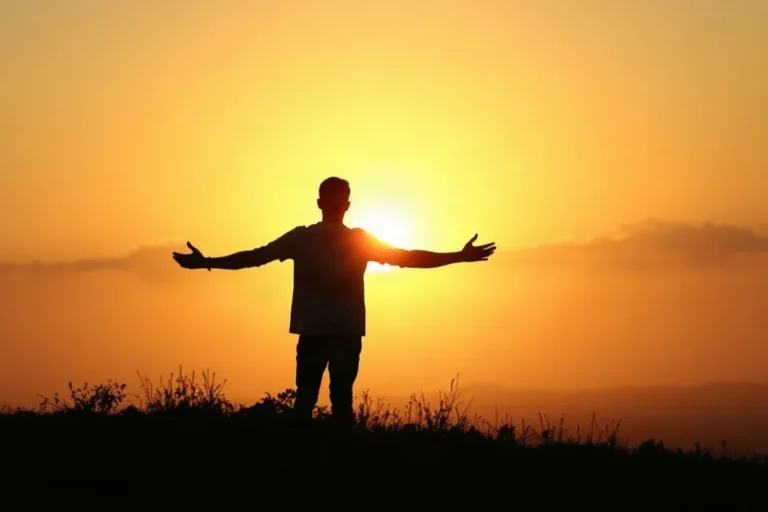 silueta de un hombre con los brazos abiertos mirando el atardecer